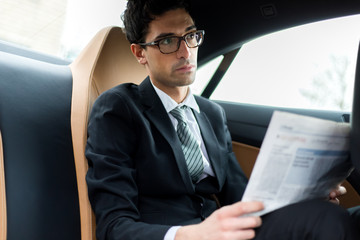Young manager reading a newspaper in the back seat of a car