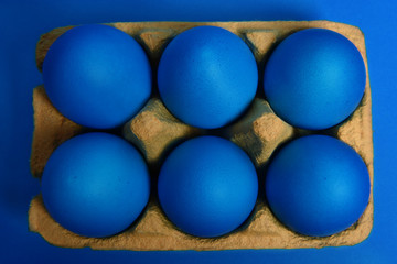 Six blue painted Easter eggs in yellow wrapping on blue background. Happy Easter holiday card or banner. Top view.