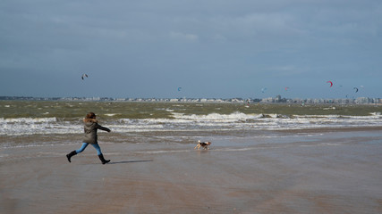 Fototapeta na wymiar A woman runs after her dog on the beach in winter