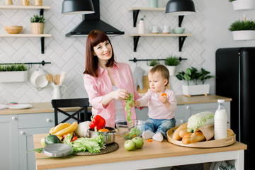 Mother and little daughter at the dining table prepare a morning Breakfast of fresh vegetables. Mom and kid preparing fresh salad together, putting green lettuce into glass bowl