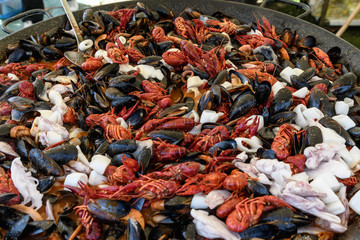 Mixed seafood cooked in a large traditional black fry pan at a street food festival, ready to eat seafood, side view, calamari, crabs, mussels with sauce