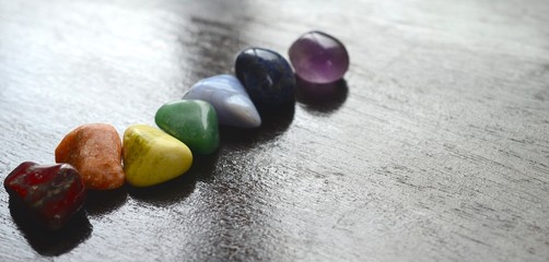 Rainbow Healing Crystals on wood table. Natural lighting with macro lens, rainbow stones. Red Jasper, Orange Calcite, Serpentine, Green Quartz, Blue Lace Agate, Sodalite, Amethyst. 
