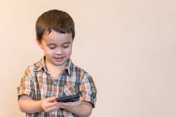 Portrait of a smiling little boy holding mobile phone isolated over light background. cute kid playing games on smartphone. copy space