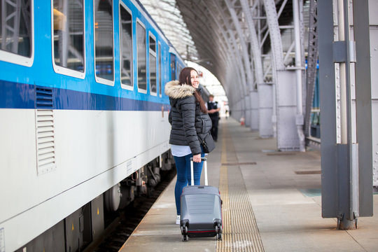 Pretty young woman with luggage waiting at the traint station for her train, transportation concept