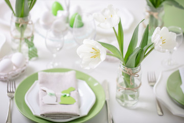 Decor and table setting of the Easter table with white tulips and dishes of green and white color. Easter decor in the form of Easter bunnies  green color with white polka dots.
