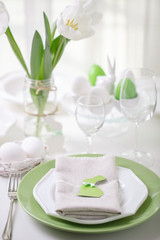 Decor and table setting of the Easter table with white tulips and dishes of green and white color. Easter decor in the form of Easter bunnies  green color with white polka dots.