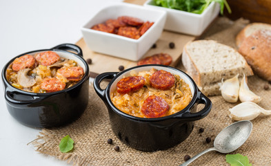 Slovak Christmas national cabbage soup in two small black pots with sausage on the jute background.