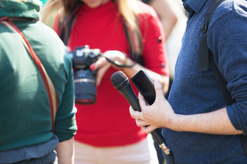 Reporter at media event holding microphone, blurred female photographer in the background