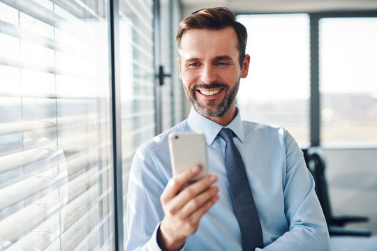 Happy Businessman Checking His Phone Standing In Modern Office