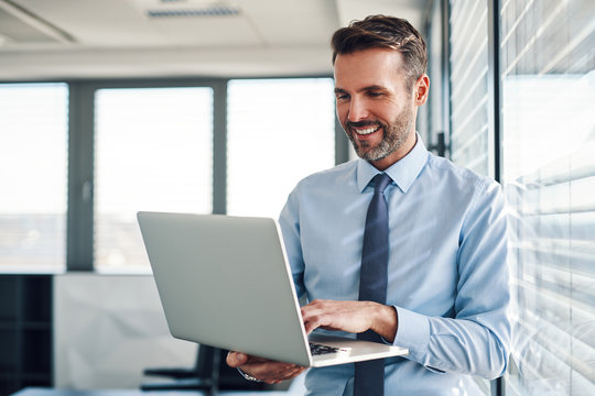 Businessman in modern office working on laptop - Powered by Adobe