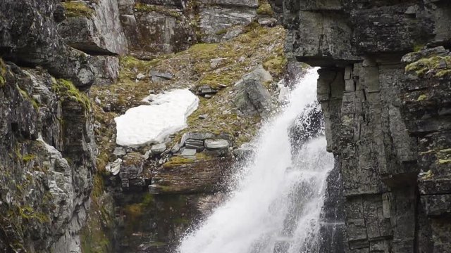 closeup of Jutulhogget Waterfall at the Rondane Nationalpark in the Norwegian mountains in slow motion floating down in a big creek of rough granit stone covered in moss, fern, ice and snow in Norway.