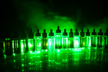 Naklejka premium Vape concept. Smoke clouds and vape liquid bottles on dark background. Light effects. Useful as background or electronic cigarette advertisement.