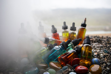 Vape concept. Beautiful colorful vape liquid glass bottles outdoor on stones. Useful as background...