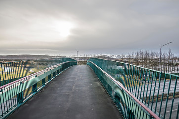 Pedestrian and bicycle bridge with an asphalt surface across a highway near Reykjavik, Iceland under a cloudy sky