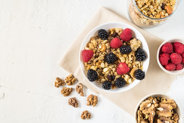 Organic granola with fresh berries and cashew nuts on white background flat lay.