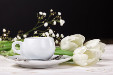 Fototapeta na wymiar Cup of coffee and white tulips on a dark background. The concept of serving Breakfast coffee on mother's Day. Cafe menu