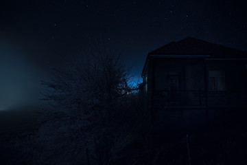 Old house with a Ghost in the forest at night or Abandoned Haunted Horror House in fog. Old mystic building in dead tree forest. Trees at night with moon.