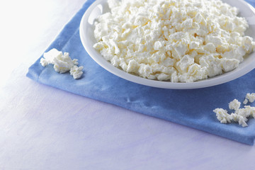 Cottage cheese on blue napkin. Cheese on white plate with wooden spoon. Soft cheese for diet. Healthy dairy product for breakfast