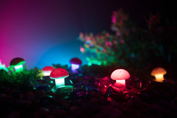 Fantasy glowing mushrooms in mystery dark forest close-up. Beautiful macro shot of magic mushroom or souls lost in avatar forest. Fairy lights on background with fog.