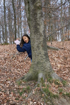 Jeune fille enfant asiatique cach&eacute;e derri&egrave;re un arbre faisant coucou d'une main