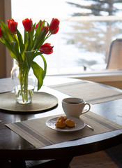 Table setting for one with dessert and a cup of coffee with bouquet of red tulips in the vase