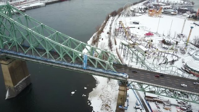 Cinematic static drone / aerial footage showing cars on Jacques Cartier Bridge and La Ronde amusement park on the background in Montreal, Quebec, Canada during winter season.
