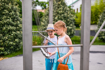 Blonde girl in white and blue dress playing in the playground in the summer park of entertainments