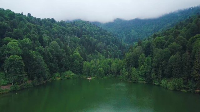 4K drone dolly forwards and upwards shot, in slow motion, over amazing Lake Karagol, reflecting trees and sky, foggy mountains in the background, in Borcka District, Artvin Province, Turkey