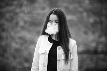 Vape teenager. Young pretty white girl in white cardigan smoking an electronic cigarette opposite...