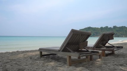 A pair of wooden sun loungers on a sandy beach overlooking the sea. - Powered by Adobe