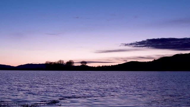 Purple rippling lake with silhouette mountain skyline in colorful sunset