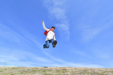 青空でジャンプする小学生の女の子（ランドセル）