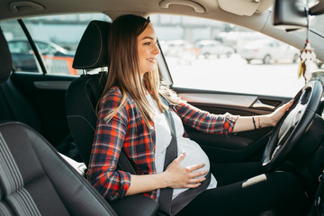 Pregnant happy woman driving with safety belt on in the car.
