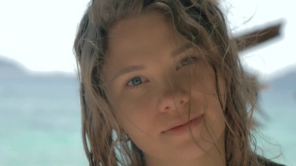 Close-up portrait of beautiful european young woman looking in the camera, hair blowing in wind on tropical beach, blue sea on the background. Travel concept.