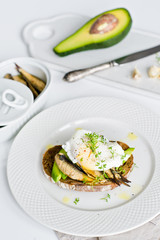 Black bread sandwich with avocado, poached egg and sprats. White background, side view.