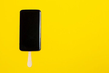 Mobile phone on a stick looks like a delicious chocolate popsicle dessert, with copy space,  on a bright yellow background. Concept of sweet life. Close-up.