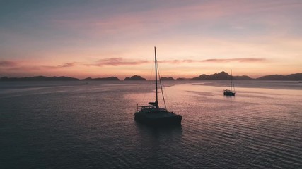 Aerial drone view of sailing yacht anchored in the bay with clear and turquoise water on the sunset. Sailing yacht in the tropical lagoon. Tropical landscape. El Nido, Palawan island, Philippines.