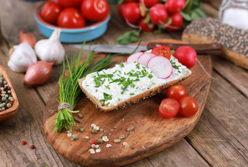 healthy breakfast -  wholemeal roll with quark and fresh chives, radishes and tomato on a rustic wooden table - healthy breakfast