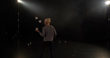 4k - Juggler in the black studio makes tricks with five balls.