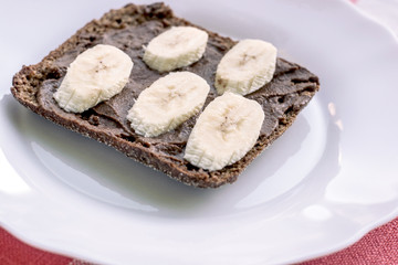 Healthy rye bread with carob and banana on the white plate. Healthy concept.