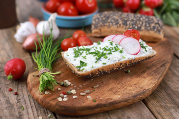 Fototapeta na wymiar healthy breakfast - wholemeal roll with quark and fresh chives, radishes and tomato on a rustic wooden table - healthy breakfast