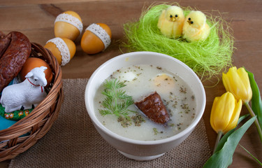 Wielkanocne śniadanie - żurek z jajkiemi i kiełbasą, obok pisanki, koszyczek ze świeconką