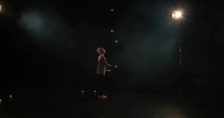4k - Juggler in the black studio makes tricks with five balls.