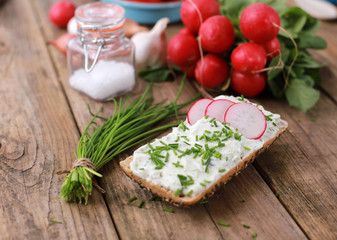 healthy breakfast - wholemeal roll with quark and fresh chive, radish  on a rustic wooden table 