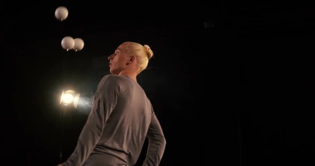 Juggler in the black studio makes tricks with five balls