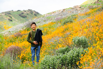 Young sporty Asian boy enjoying & hiking the mountain during the California Golden Poppy and Goldfields blooming in Walker Canyon, Lake Elsinore, CA. USA. Asian kid making his way through the mountain
