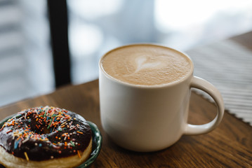 Coffee with a drawn heart and milk on a wooden table in a coffee shop. Pink donut with scattering...