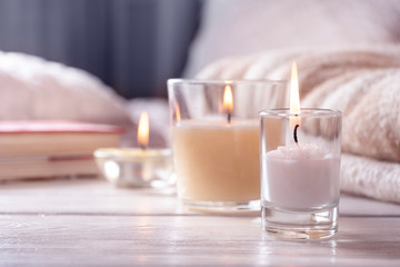 Home interior. Still life with detailes. Several candles on white wooden table in front of bed, the concept of cosiness.