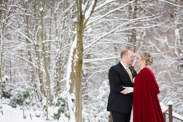 Stunning bride and groom embracing in snow covered woods