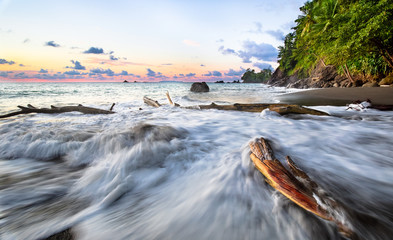 Long exposure of waves crashing against driftwood at sunset on the west coast of the Osa Peninsula, Costa Rica.